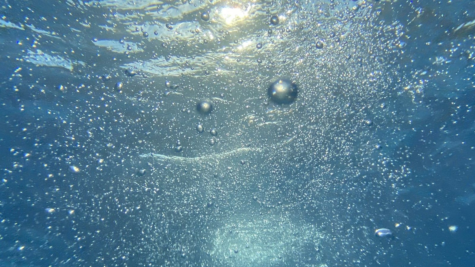 Air bubbles rising through clear blue water
