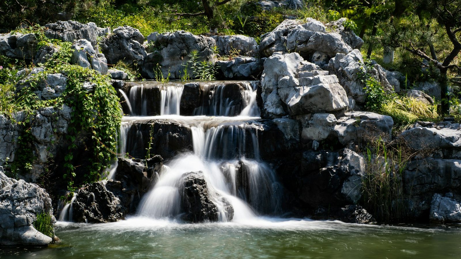 Rock waterfall cascading into a garden pond surrounded by trees