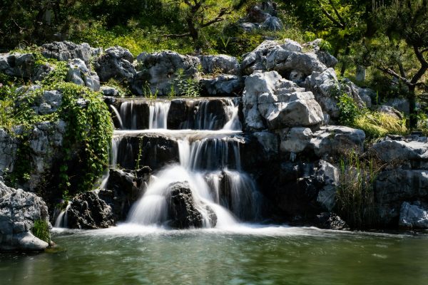 Rock waterfall cascading into a garden pond surrounded by trees